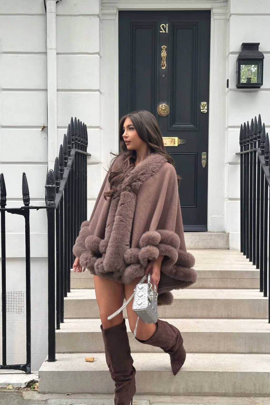 Woman wearing a fur coat and knee-high boots standing on steps in front of a building entrance.