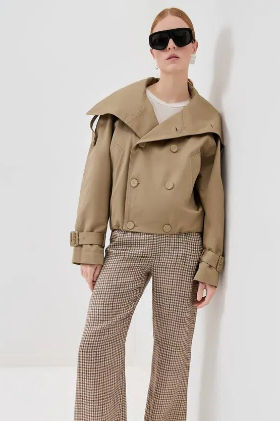 Person wearing a beige trench coat and plaid pants against a white background