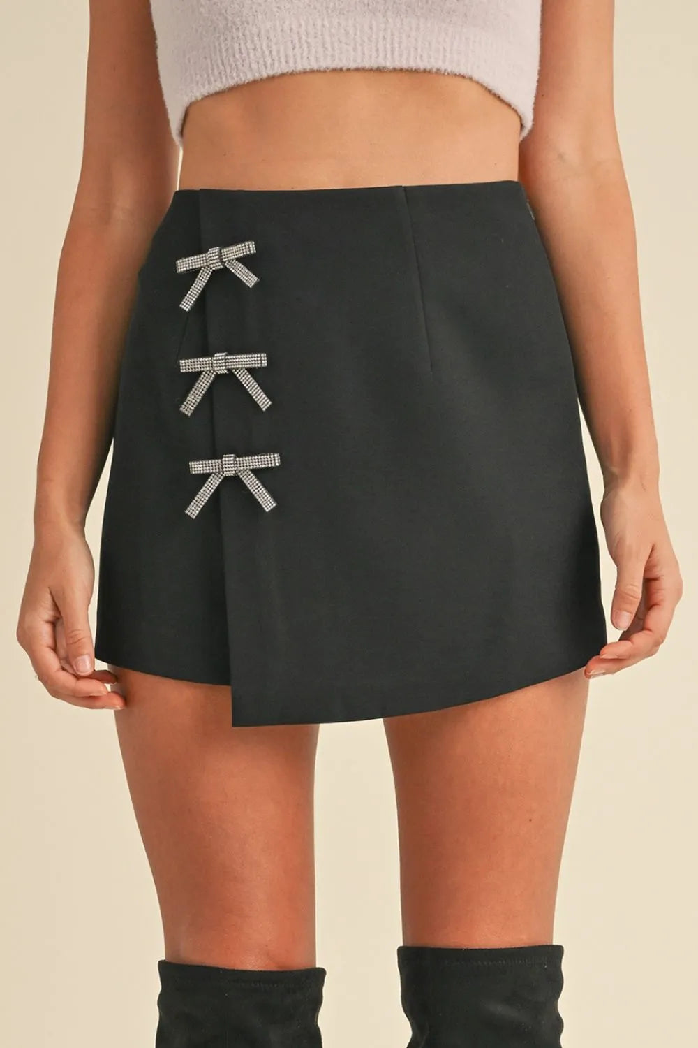 Black mini skirt with bow details worn by a person on a beige background