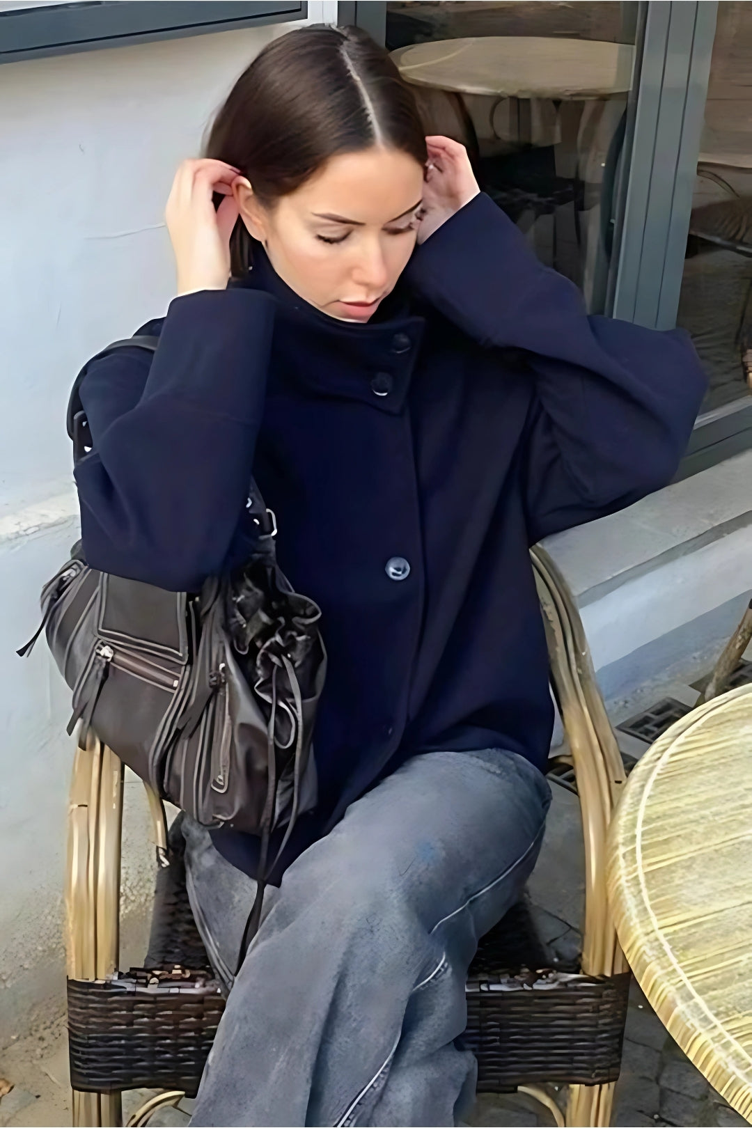 Woman in a navy pea coat sitting outdoors with a handbag.