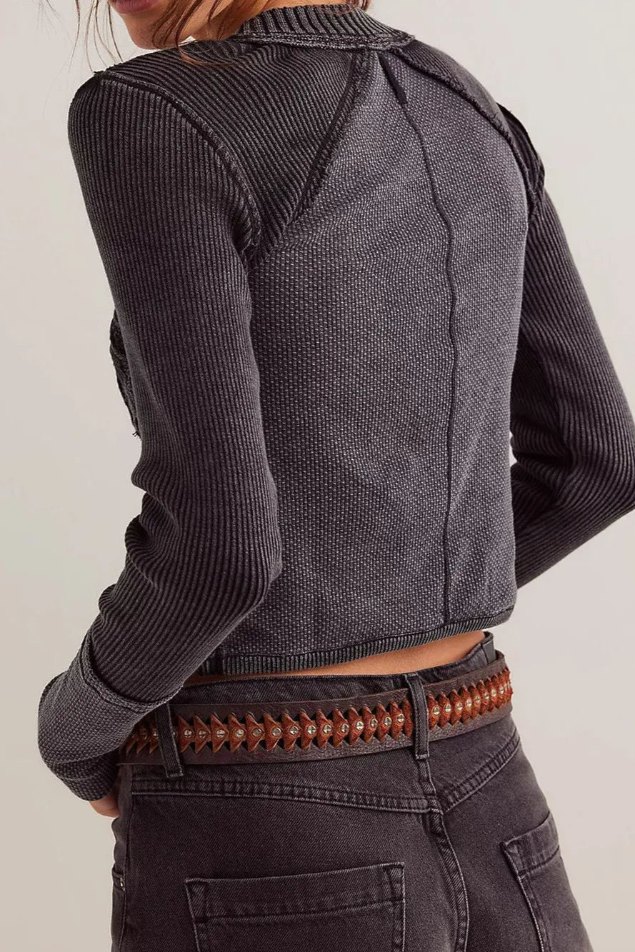 Person wearing a dark ribbed sweater and jeans with a brown belt on a light background